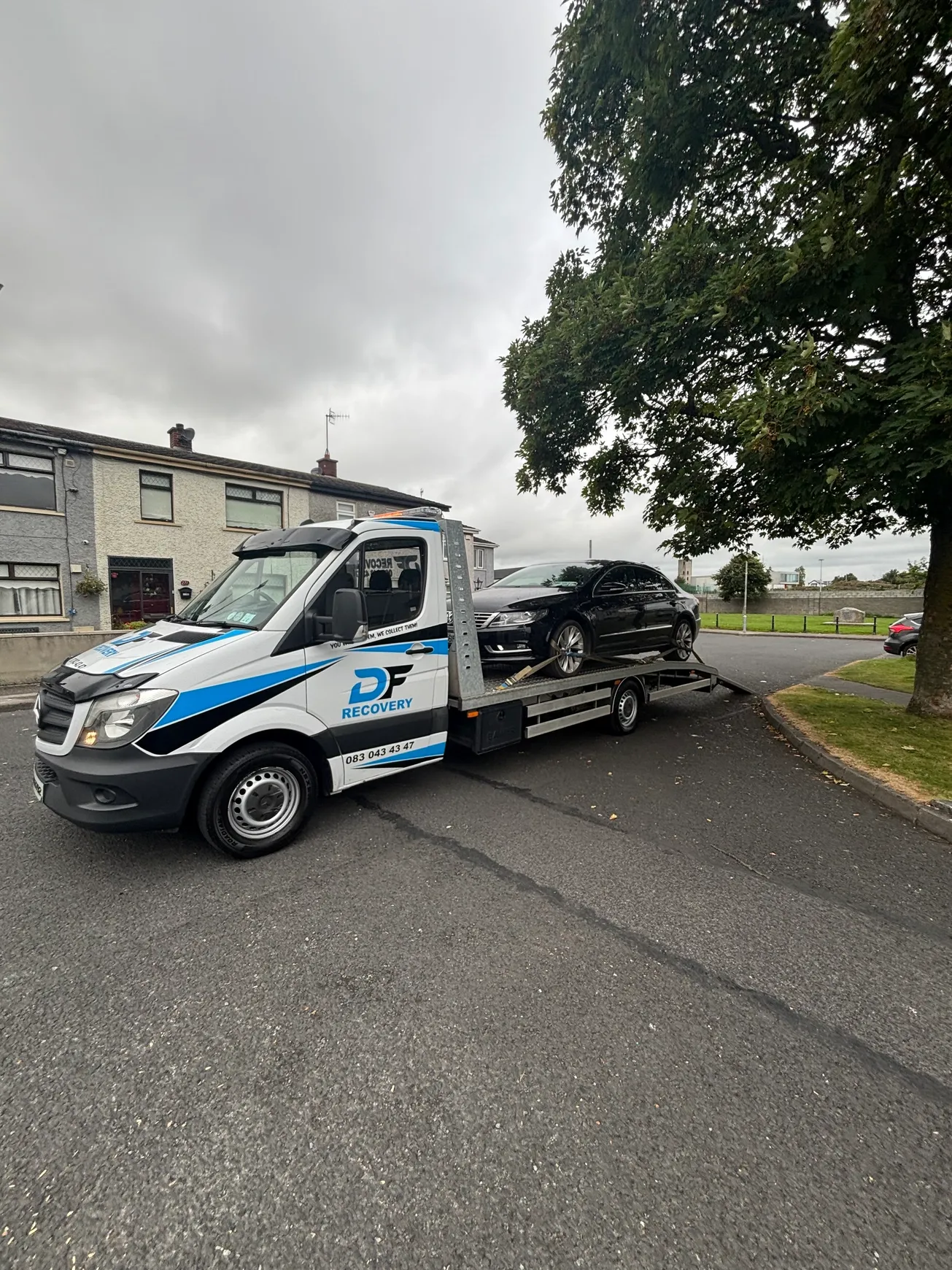 DF Recovery flatbed collecting a black Volkswagen on a residential street.